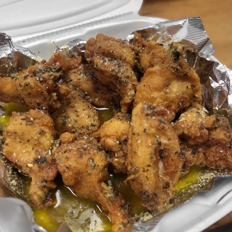 Close-up of crispy fried chicken wings seasoned with herbs and spices, resting in a takeout container.