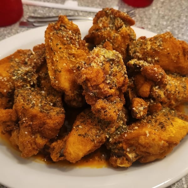 Close-up of crispy fried chicken wings coated in herbs and Parmesan cheese, with sauce pooling below.