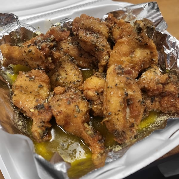 Close-up of crispy fried chicken wings with herbs and cheese, served in a foil-lined container.