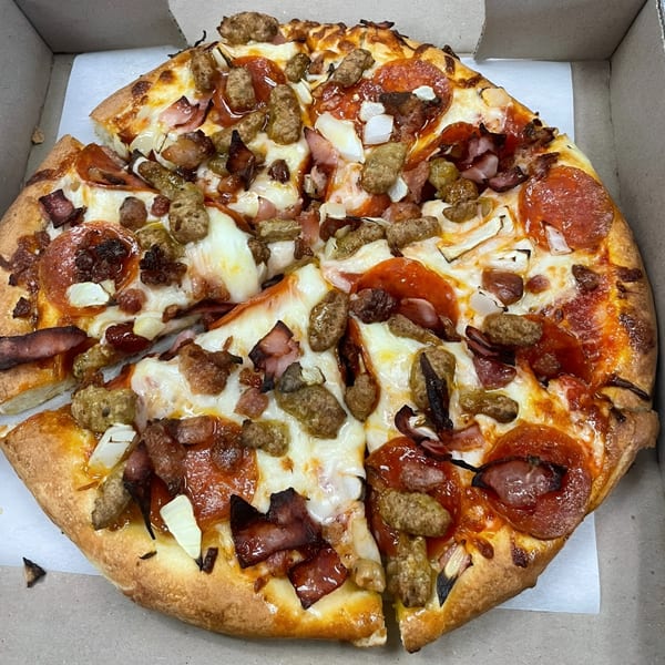 A whole meat lover's pizza with pepperoni, sausage, bacon, and onions in a cardboard box.