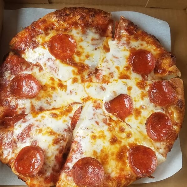 A whole pepperoni pizza, cut into slices, sits in a cardboard delivery box.