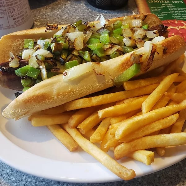 A sausage sandwich with grilled onions and green peppers, served with a side of french fries.