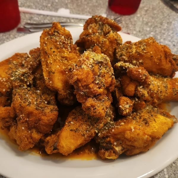 A plate of crispy, golden-brown chicken wings coated in herbs and Parmesan cheese.