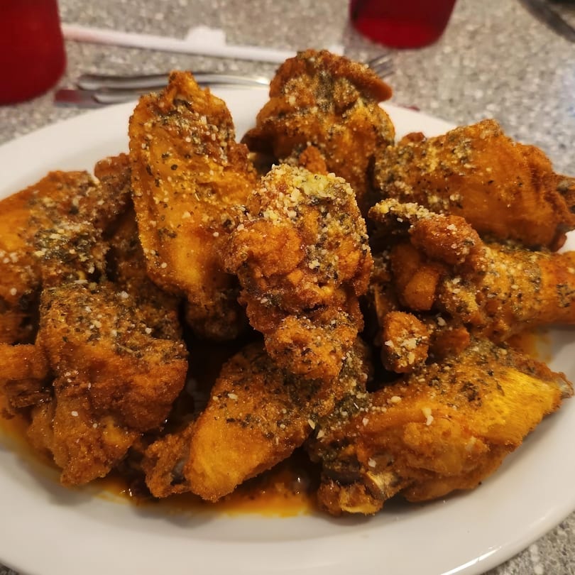 A plate of crispy, golden-brown chicken wings coated in herbs and Parmesan cheese.