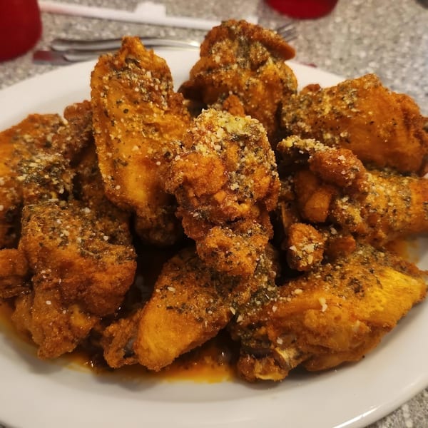 A plate of crispy, golden-brown chicken wings coated in herbs and parmesan cheese, with sauce pooling below.