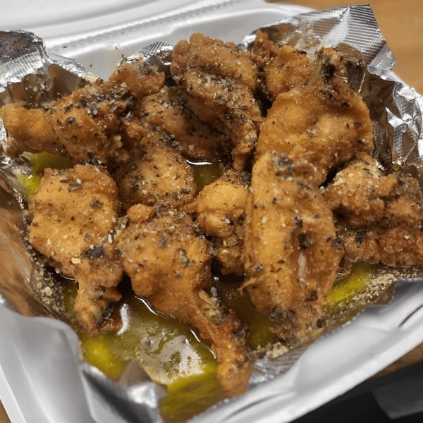 Crispy fried chicken wings seasoned with herbs and spices, served in a foil-lined takeout container.