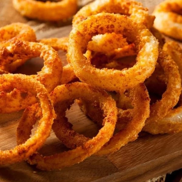 Golden brown, crispy onion rings piled on a rustic wooden board.