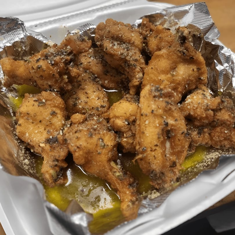Crispy fried chicken wings, seasoned with herbs and spices, served in a foil-lined takeout container.