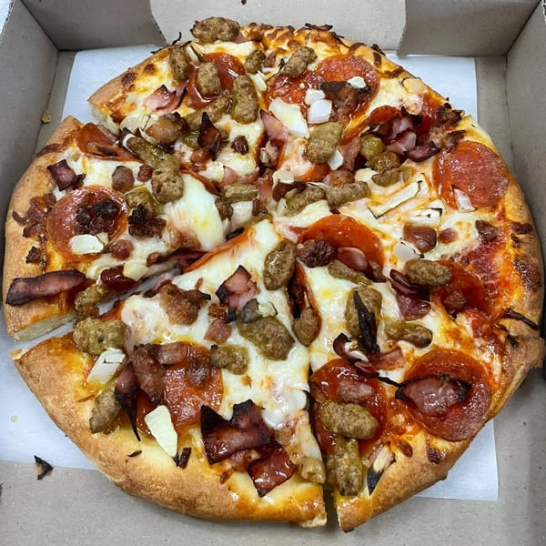 A whole meat lover's pizza with pepperoni, sausage, bacon, and onions in a cardboard box.