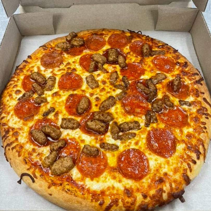 A whole pepperoni and sausage pizza in a cardboard box, with melted cheese and a golden crust.